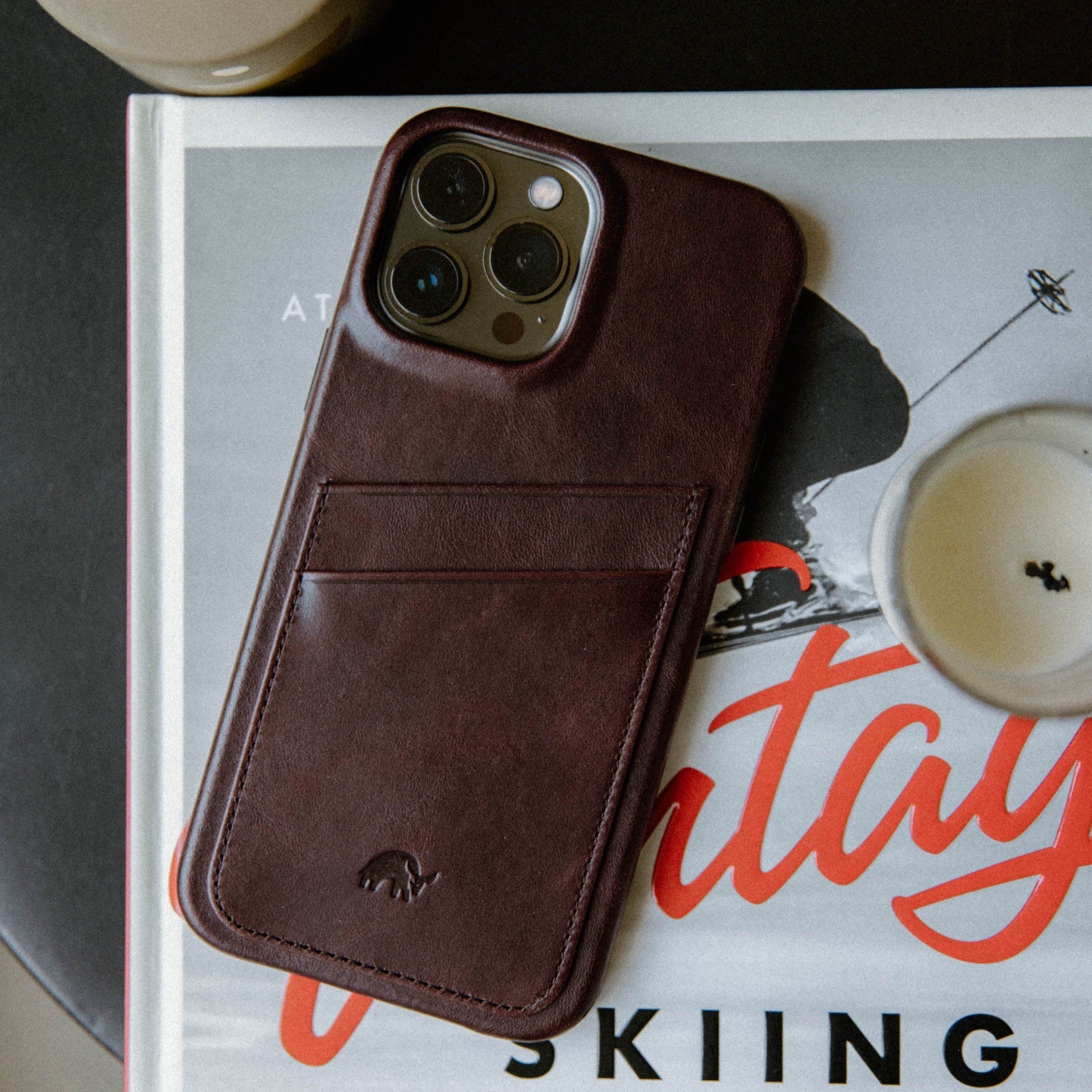 The Minimalist Portfolio Case in Bourbon color, featuring a card slot, placed on a book with a candle nearby.