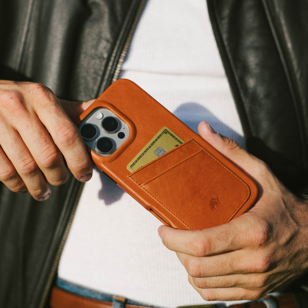 Sienna leather phone case with external card pocket holding a card, held by person in white shirt and leather jacket