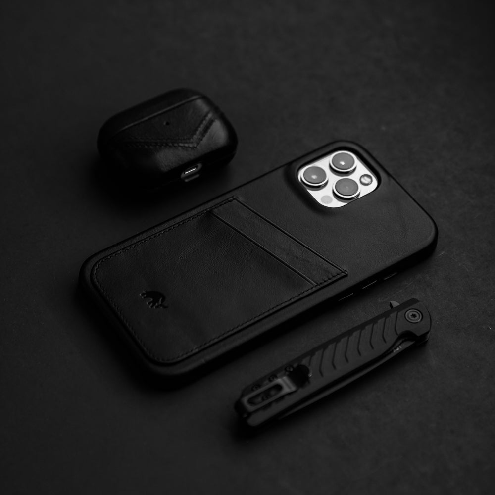 A black minimalist portfolio case with card slot, an AirPods case, and a knife on a dark surface.