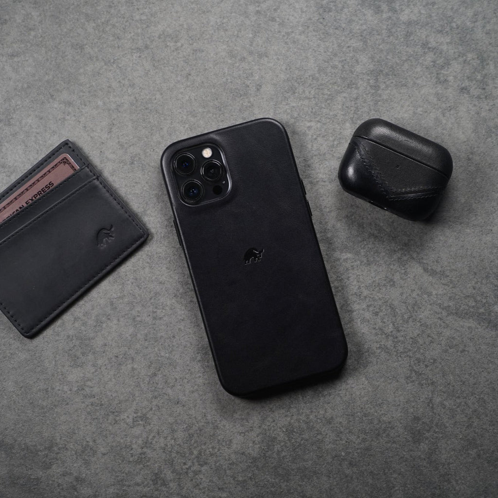 Black leather AirPods case next to a phone and wallet on a gray surface.