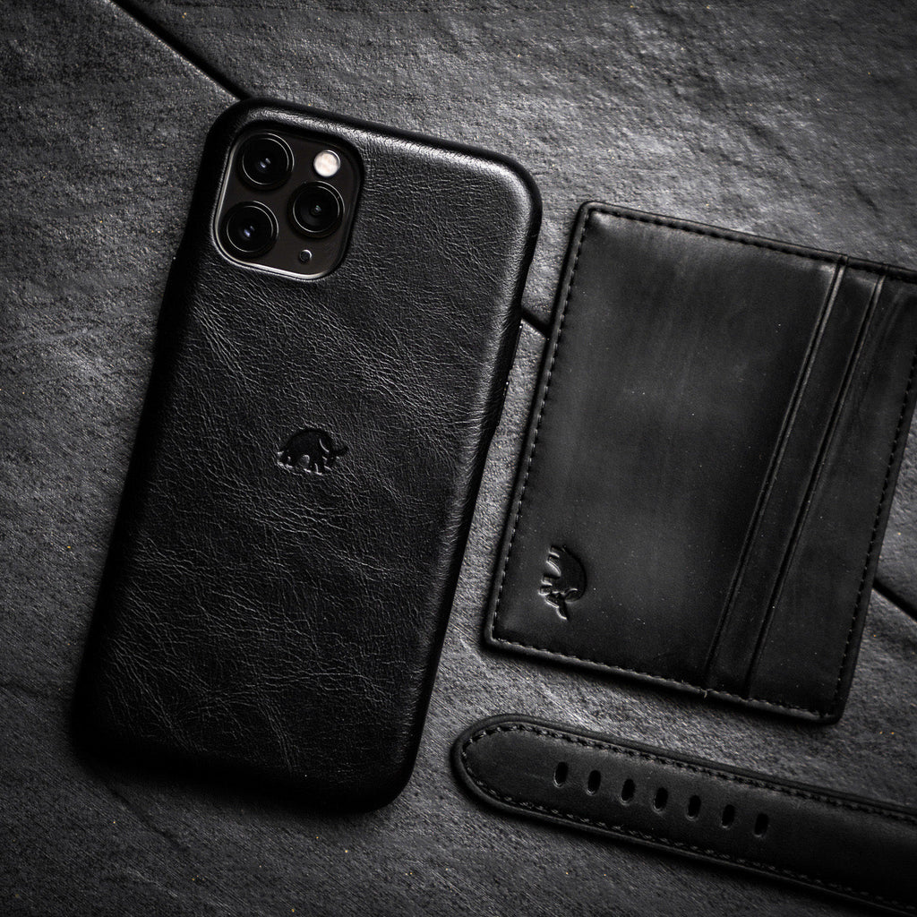 Black leather card holder next to a phone case and strap on a dark surface