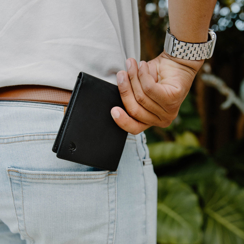 A person placing a black bifold wallet into their back pocket.